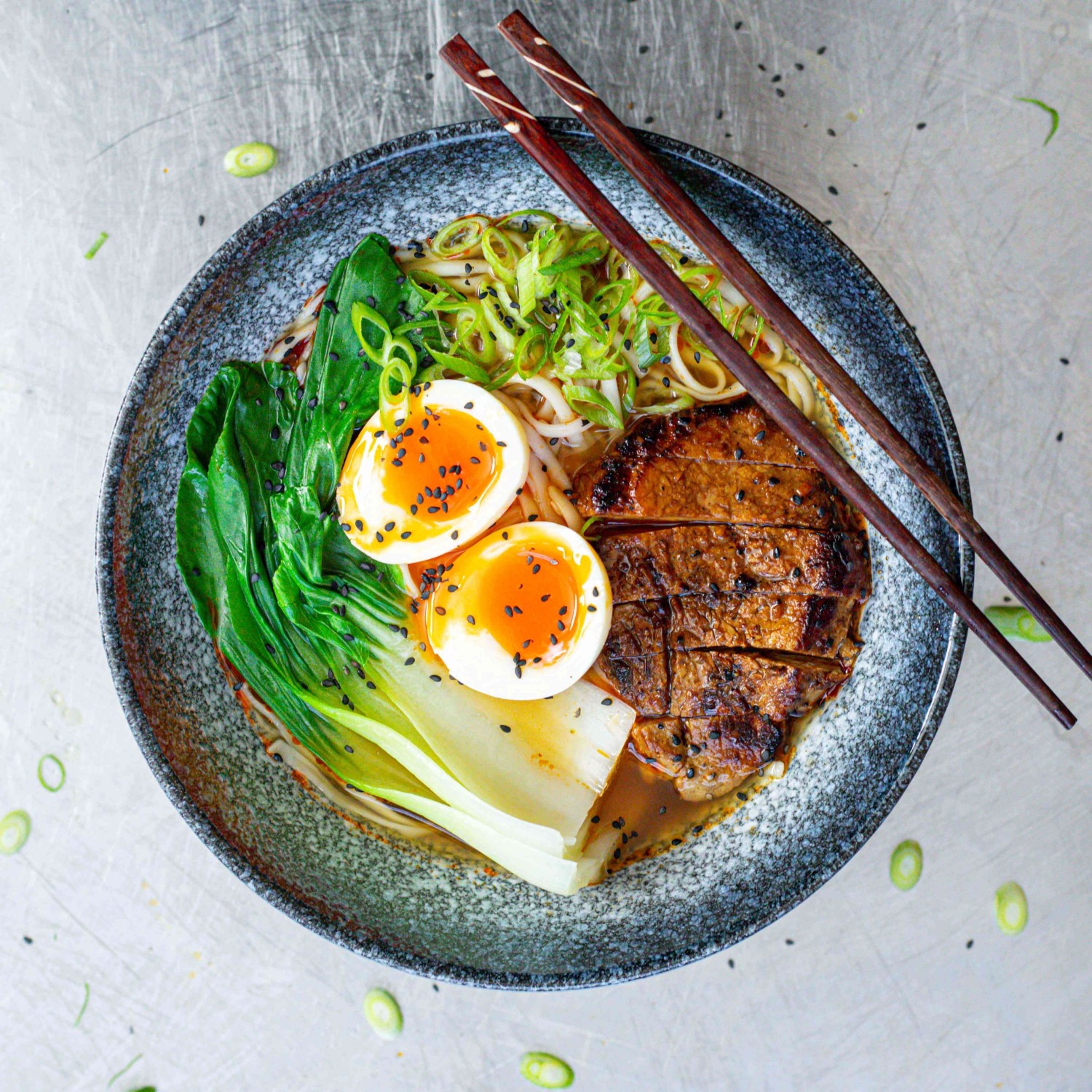 A bowl of ramen with pork, pak choi and a soft boiled egg.